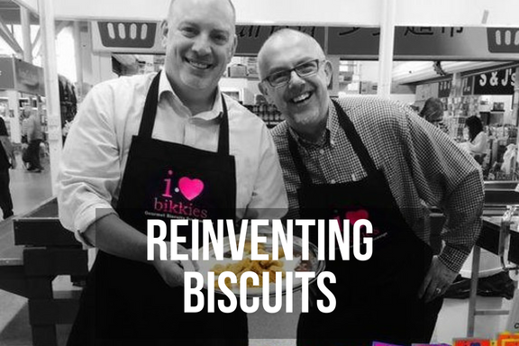 A pair of smiling men in aprons selling cookies at a market with headline 'reinventing biscuits'